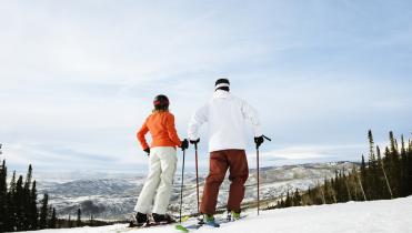 Two people skiing down a snowy slope on a sunny day.